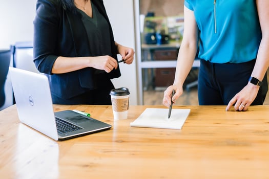 Two women discussing a paper document on a table with a laptop