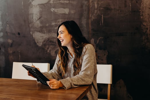 Girl sitting at a table smiling and holding a tablet.