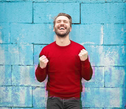 Man in red shirt cheering in front of blue brick wall.