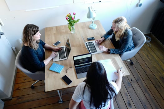 Three women typing on laptops and sitting around a table