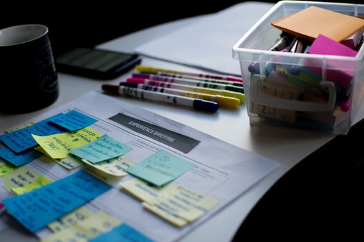 Sticky notes attached to a piece of paper next to markers on a table