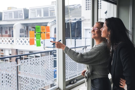 Two women looking at sticky notes stuck on a window