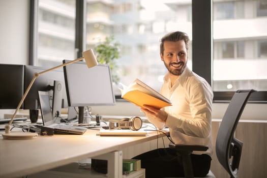 Business man sitting at a desk holding a notebook.